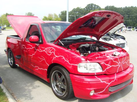 2007 Ford Mustang - A red pickup truck with a custom lightning bolt paint job is displayed with its hood and bed open.