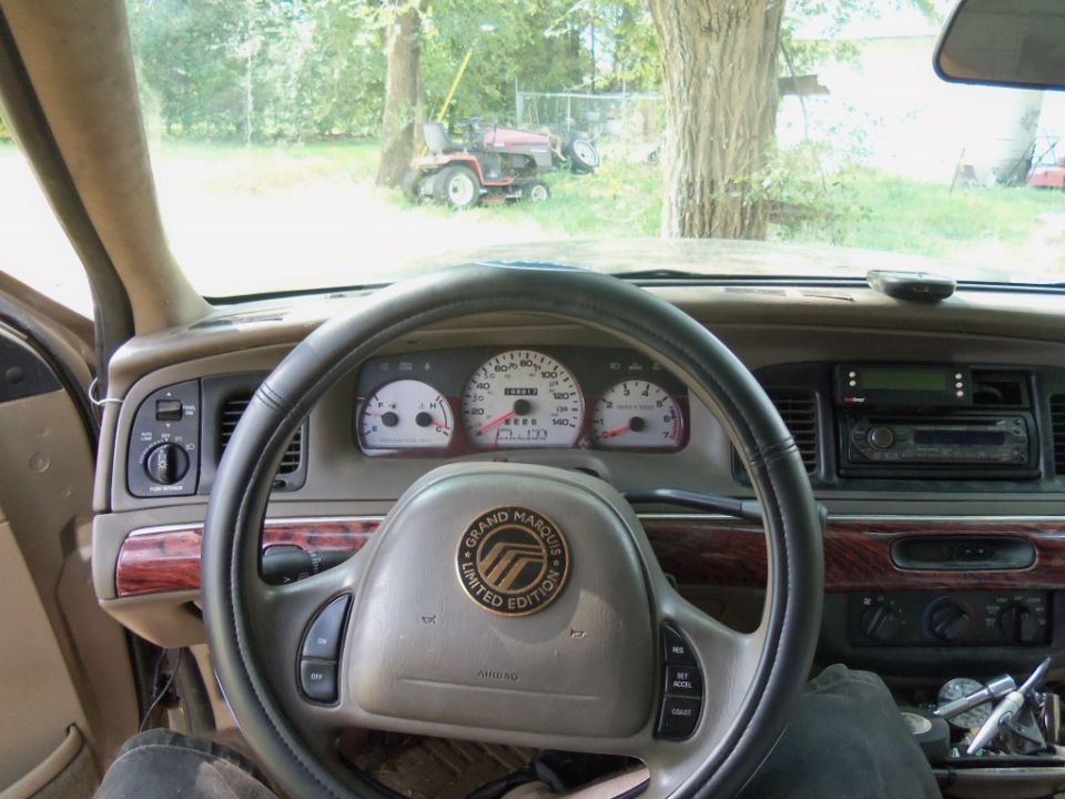 Dashboard of a 2000 Mercury Grand Marquis with wood trim, showing the steering wheel, gauges, and radio
