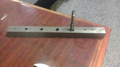 1989 Ford Bronco - A tap tool is shown inserted into a hole on a metal bar with several other holes.