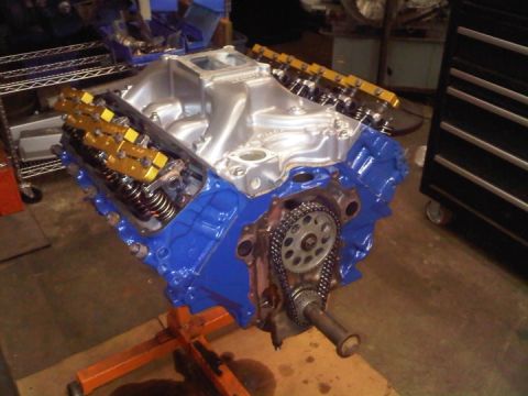 1979 Ford Bronco - Freshly assembled Ford V8 long block painted Ford blue, sitting on an orange engine stand in a shop. It has a polished aluminum intake mani…