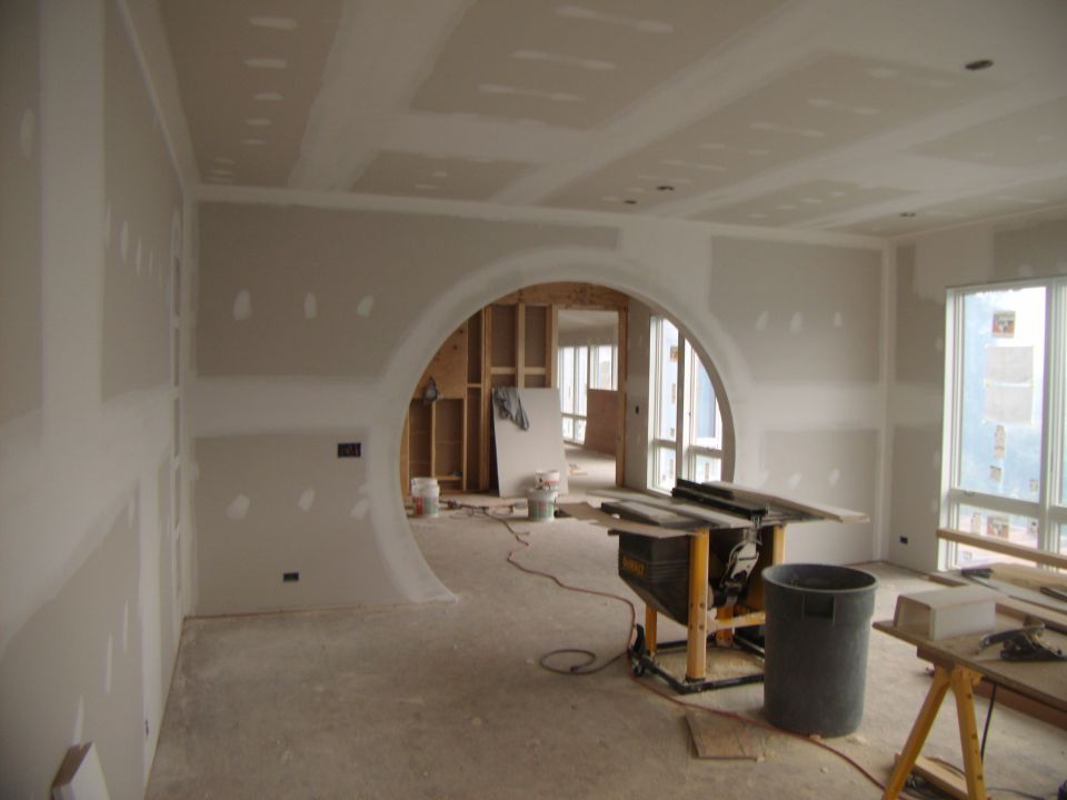 Interior construction scene with drywall, circular archway, and a table saw