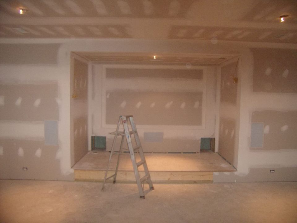 Interior construction scene with drywall, a wooden platform, and a metal ladder