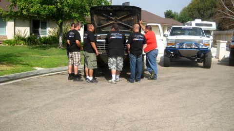 1996 Ford Bronco - Several men gather around a black Ford Bronco with its hood open, parked in a residential driveway.