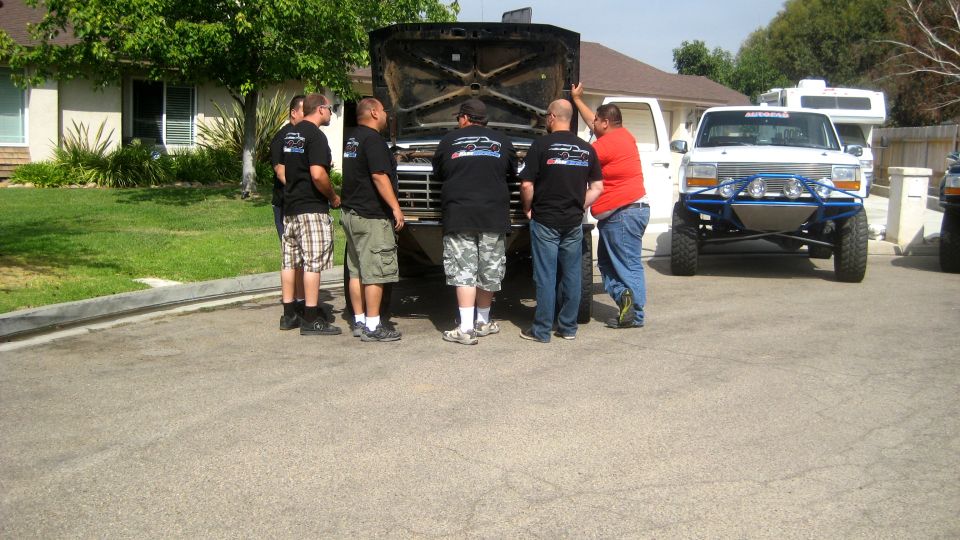 Black Ford Bronco with hood open, front view, in driveway with people around