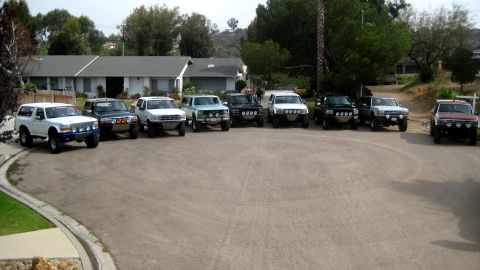 1996 Ford Bronco - A collection of modified SUVs, including a 1996 Ford Bronco, are parked in a suburban driveway.