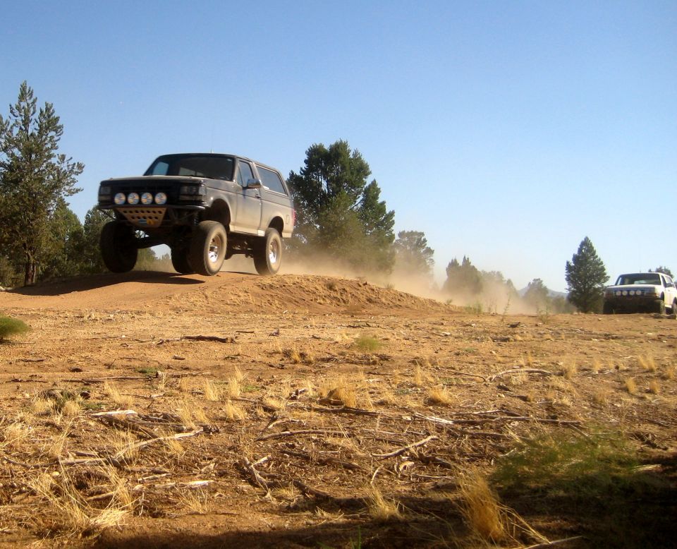 1996 Ford Bronco jumping a dirt mound with another SUV in the background