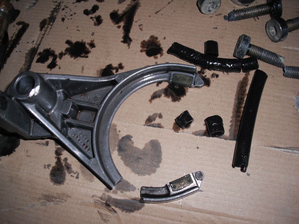 Broken metal part with black rubber pieces and bolts on a cardboard surface with oil stains