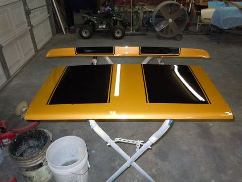 1970 Chevrolet Camaro - Gold hood and spoiler with black stripes, likely for a classic muscle car, are displayed in a workshop.
