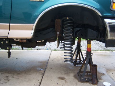 1996 Ford Bronco - The front suspension of a teal and tan Ford Bronco is disassembled and supported by jack stands.