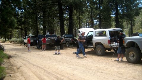 1996 Ford Bronco - Several off-road vehicles are parked on a dirt road, with people gathered around one of the Broncos.
