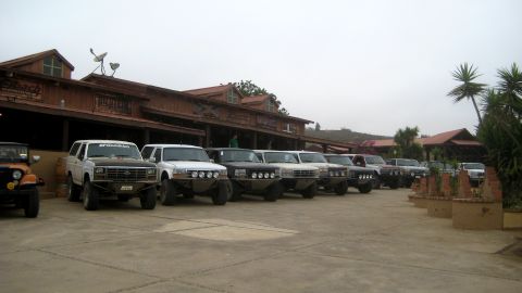 1996 Ford Bronco - Several Broncos and a Jeep are parked in a lot outside a rustic building.