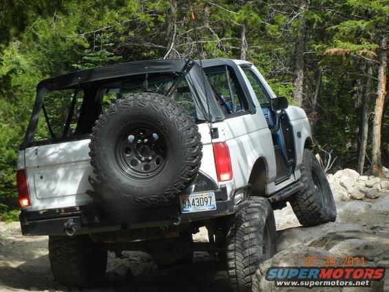White topless Ford Bronco with roll cage crawling rocks on a forest trail