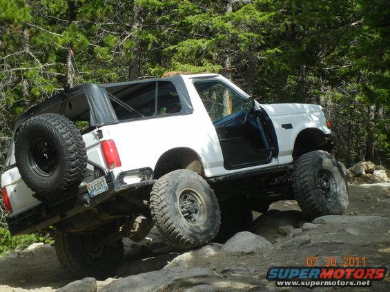White Ford Bronco with soft top and tailgate spare crawling granite rocks on a forest trail