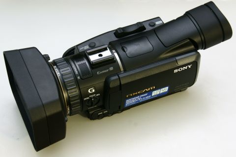 1993 Ford Taurus - A black Sony NXCAM camcorder is shown from a three-quarter front angle, highlighting its lens and microphone attachments.