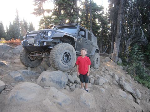 2008 Jeep Wrangler - A boy poses with a lifted Jeep Wrangler on a challenging off-road trail.