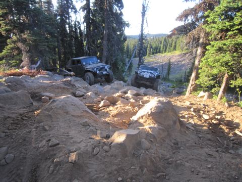2008 Jeep Wrangler - Two Jeeps tackle a challenging, boulder-strewn path in a wooded mountain area.