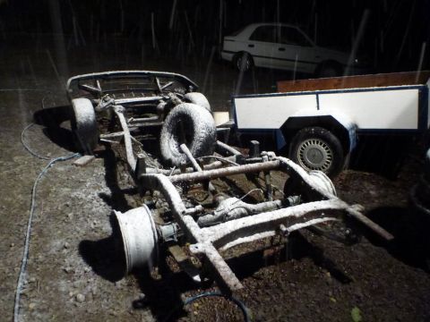 1969 Lincoln Continental - A car chassis sits in the snow next to a trailer and another vehicle, suggesting a scene of disrepair or storage.