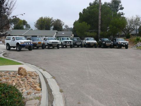 1988 Ford Bronco - A lineup of Ford Bronco SUVs, mostly from the late 1980s, are parked in a residential area.