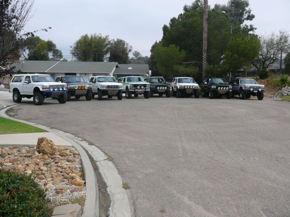 Several Ford Bronco SUVs parked in a row on a street, some modified with off-road bumpers
