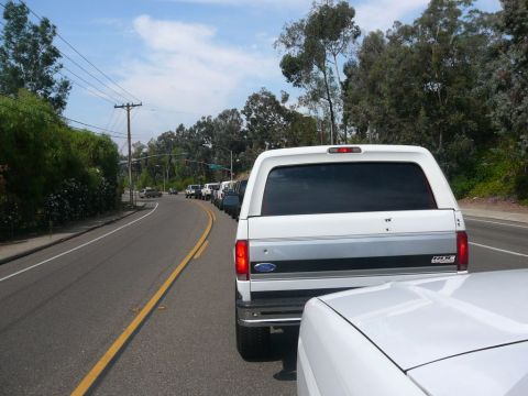 1988 Ford Bronco - A white 1988 Ford Bronco with a camper shell is seen from behind in a line of traffic on a sunny day.