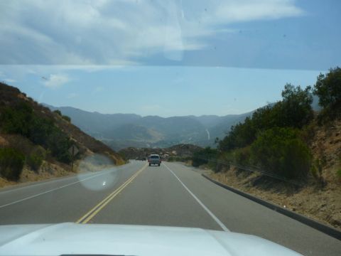 1988 Ford Bronco - A lone SUV travels down a highway winding through a scenic mountain pass on a clear day.