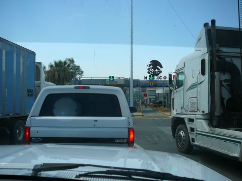 1988 Ford Bronco - A white pickup truck with a camper shell is seen from behind at a border crossing.
