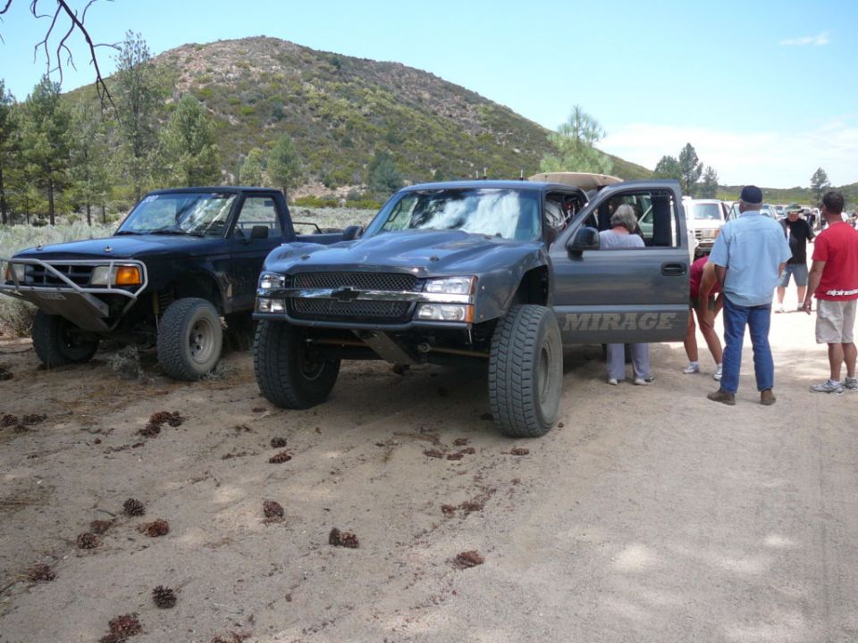 Dark gray off-road truck with a lifted suspension and large tires, door open, with a black truck behind it