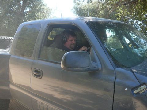 1988 Ford Bronco - A man in headphones drives a gray pickup truck, with a spare tire visible in the bed.