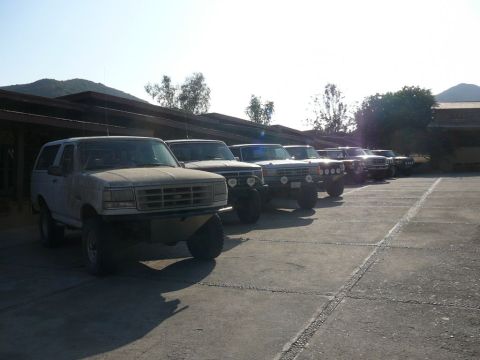 1988 Ford Bronco - A line of SUVs, including a 1988 Ford Bronco, are parked in a lot under a covered structure.
