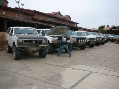 1988 Ford Bronco - Several Ford Broncos are lined up in front of a rustic building, with one man posing in the foreground.