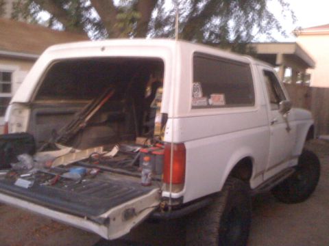 1990 Ford Bronco - A white 1990 Ford Bronco is viewed from the rear with its tailgate down, revealing tools and electrical components.