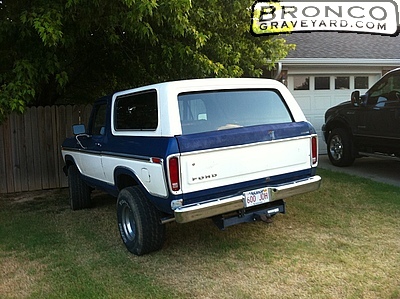 Two-tone blue and white Ford Bronco parked in a grassy yard next to a garage