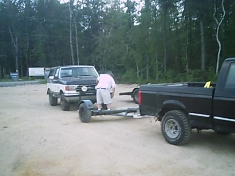 1988 Ford Bronco - A person attends to a trailer connected to a two-tone SUV, with a black pickup truck nearby.