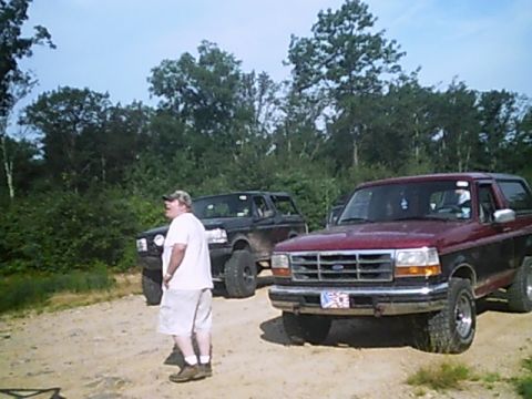 1988 Ford Bronco - A man stands near two Ford Broncos on a dirt path with trees in the background.