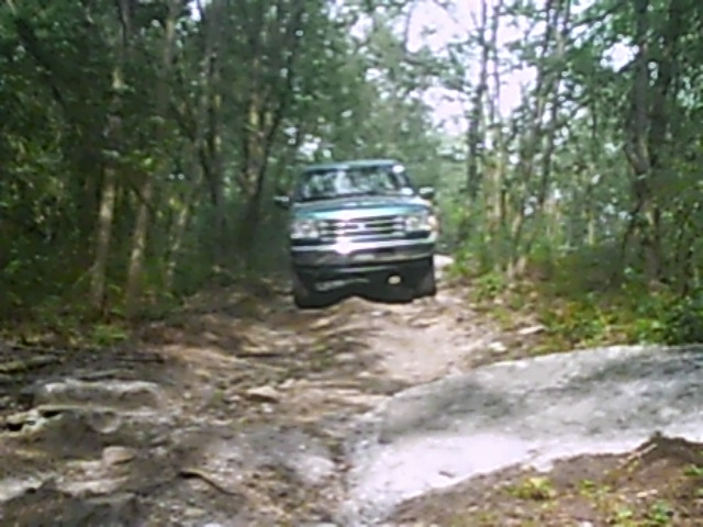 Green SUV driving on a rocky, wooded trail