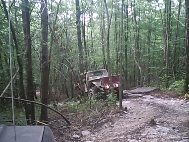 Red off-road truck with a lifted suspension navigating a rocky, wooded trail