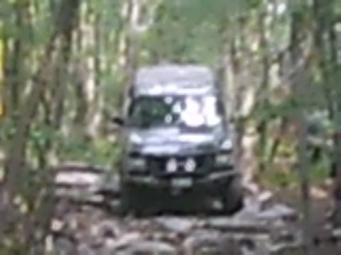1988 Ford Bronco - An off-road SUV navigates a challenging path through a dense forest.