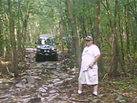1988 Ford Bronco - A man stands on a rocky path as a black SUV navigates the trail through a dense forest.