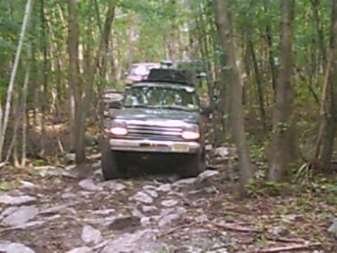1988 Ford Bronco - A 1988 Ford Bronco navigates a challenging, rocky path through a dense forest during an off-road excursion.