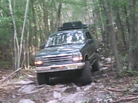 1988 Ford Bronco - SUV navigates a challenging rocky path through a dense forest.