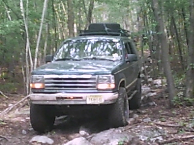 Dark green Ford Explorer on a rocky, wooded trail with a roof rack