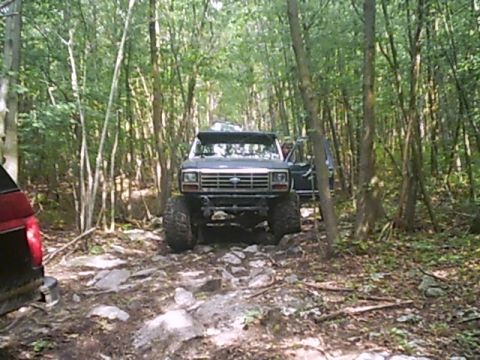 1988 Ford Bronco - A lifted Ford Bronco navigates a rocky path through a dense forest.