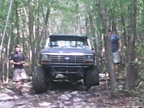 1988 Ford Bronco - Modified Ford truck navigating a rough, wooded path with two people present.