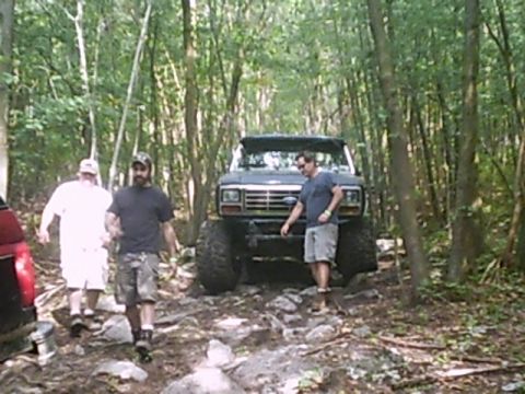 1988 Ford Bronco - A lifted Ford Bronco navigates a rocky path through a dense forest with several people around.
