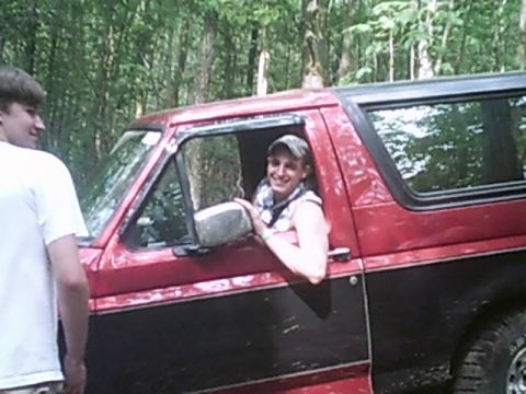 1988 Ford Bronco - A red and black 1988 Ford Bronco is seen off-road with a smiling driver and another person standing nearby.