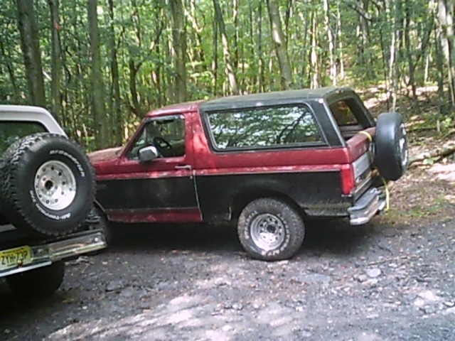 Red and black 1988 Ford Bronco, side view, with spare tire on rear