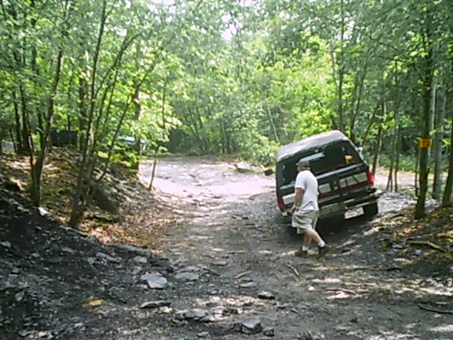 Black SUV with a man walking away from it on a rocky, wooded trail