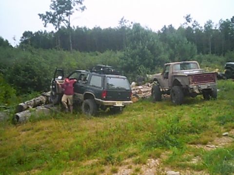 1988 Ford Bronco - Two off-road vehicles are parked in a grassy area with trees in the background.