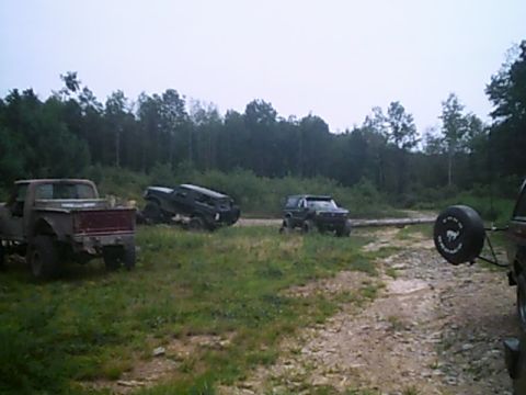 1988 Ford Bronco - Several off-road vehicles are parked on a dirt path with trees in the background.