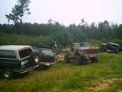 1988 Ford Bronco - A group of modified trucks and SUVs are gathered in a wooded, grassy area.